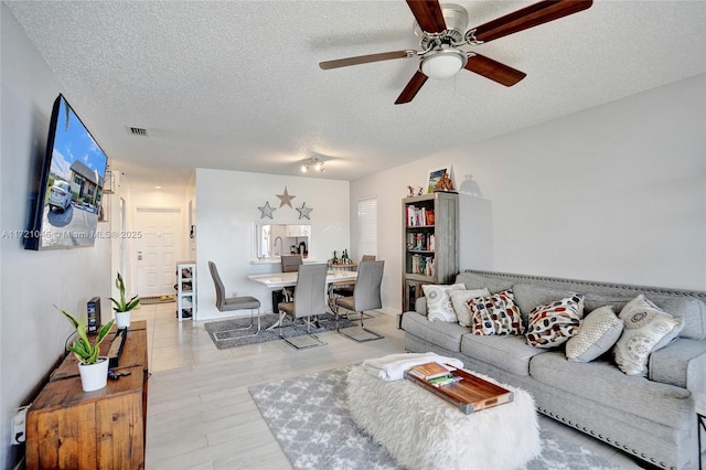 living room with a textured ceiling, light hardwood / wood-style floors, and ceiling fan