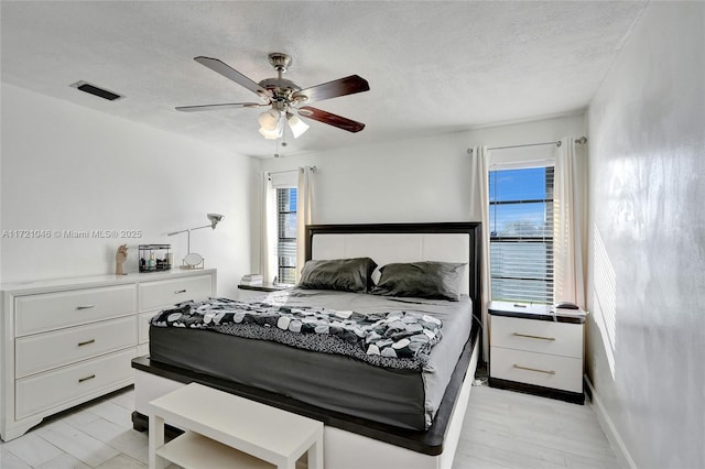 bedroom featuring ceiling fan, light hardwood / wood-style floors, and a textured ceiling