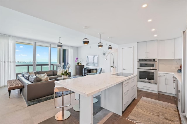 kitchen with white cabinetry, stainless steel double oven, hanging light fixtures, tasteful backsplash, and a water view