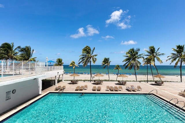 view of swimming pool featuring a water view, a beach view, and a patio