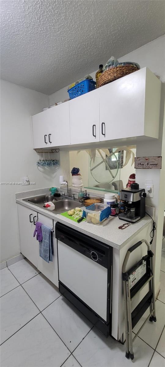 kitchen featuring sink, light tile patterned flooring, white dishwasher, a textured ceiling, and white cabinets