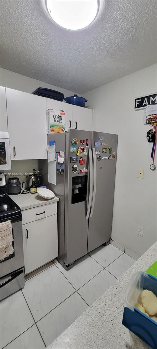 kitchen featuring white cabinets, light tile patterned flooring, a textured ceiling, and appliances with stainless steel finishes