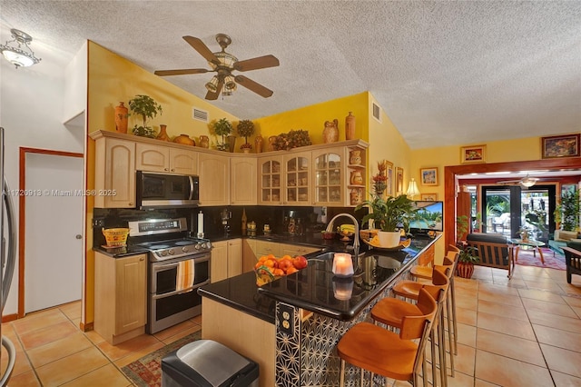 kitchen featuring sink, lofted ceiling, a breakfast bar, light tile patterned floors, and appliances with stainless steel finishes