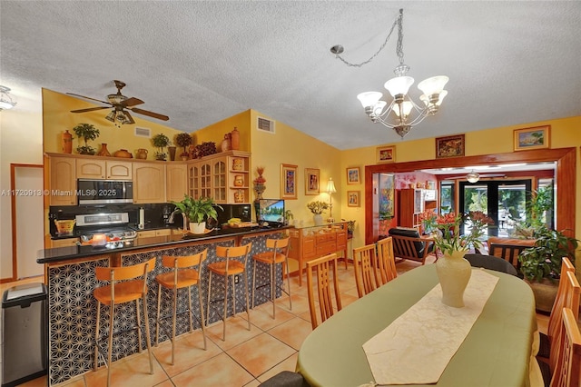 dining area with ceiling fan with notable chandelier, light tile patterned floors, a textured ceiling, and vaulted ceiling