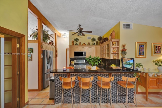 kitchen featuring a breakfast bar, kitchen peninsula, appliances with stainless steel finishes, and vaulted ceiling