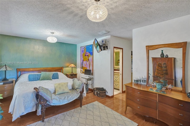 bedroom featuring ensuite bath, an inviting chandelier, a textured ceiling, and light hardwood / wood-style flooring