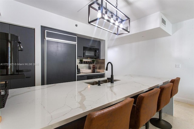 kitchen featuring a kitchen breakfast bar, light stone counters, sink, paneled built in refrigerator, and hanging light fixtures