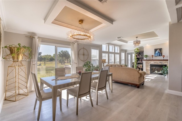 dining area with a tray ceiling, crown molding, an inviting chandelier, and light wood-type flooring