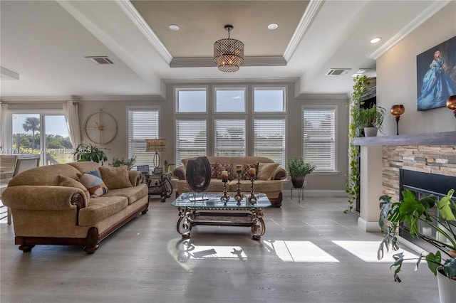 living room with a raised ceiling, a wealth of natural light, a fireplace, and ornamental molding