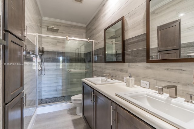 bathroom featuring vanity, crown molding, toilet, tile walls, and a shower with shower door