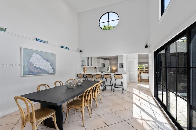 dining room with a towering ceiling, a healthy amount of sunlight, and light tile patterned flooring