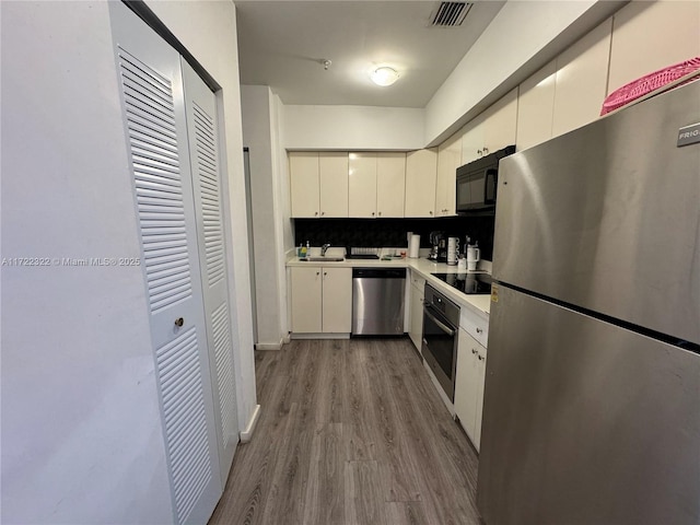 kitchen with black appliances, white cabinets, sink, light hardwood / wood-style flooring, and decorative backsplash