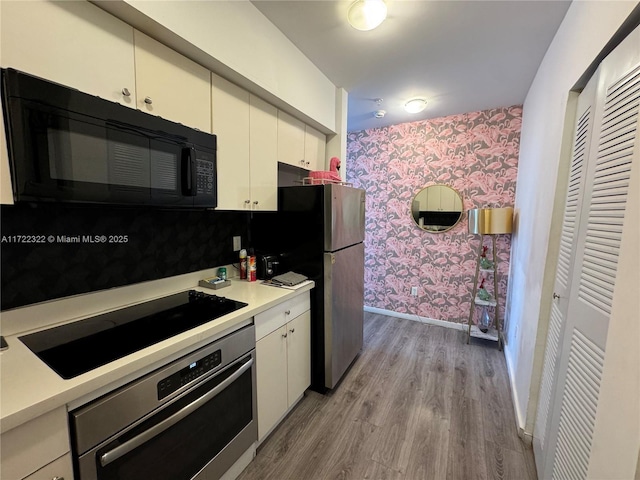 kitchen with white cabinets, decorative backsplash, stainless steel appliances, and light hardwood / wood-style flooring