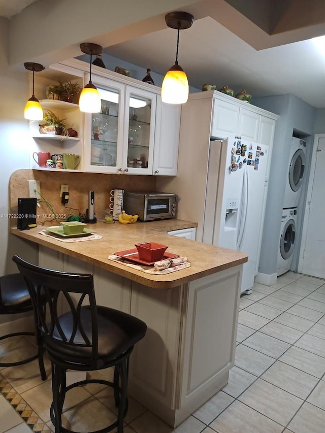 kitchen featuring a breakfast bar, white refrigerator with ice dispenser, kitchen peninsula, white cabinetry, and stacked washer / dryer