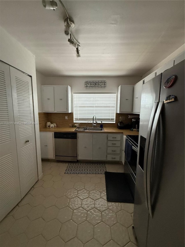 kitchen with backsplash, track lighting, stainless steel appliances, sink, and white cabinetry