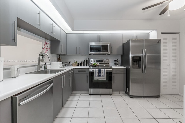 kitchen featuring gray cabinetry, a sink, stainless steel appliances, light countertops, and light tile patterned floors