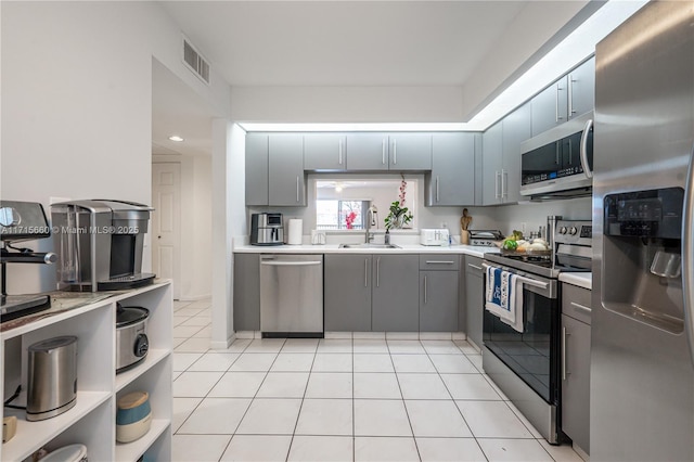 kitchen with appliances with stainless steel finishes, light tile patterned floors, gray cabinetry, and sink