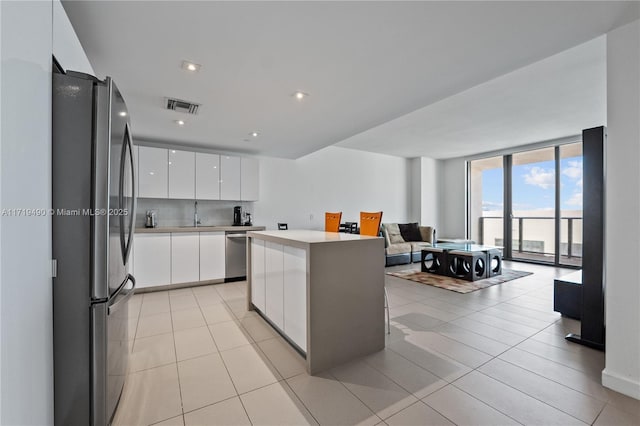 kitchen featuring floor to ceiling windows, light tile patterned floors, a kitchen island, white cabinetry, and stainless steel appliances