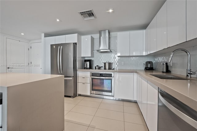 kitchen featuring decorative backsplash, wall chimney exhaust hood, stainless steel appliances, sink, and white cabinetry