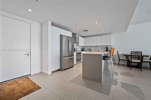 kitchen with a kitchen breakfast bar, stainless steel appliances, wall chimney range hood, a center island, and white cabinetry