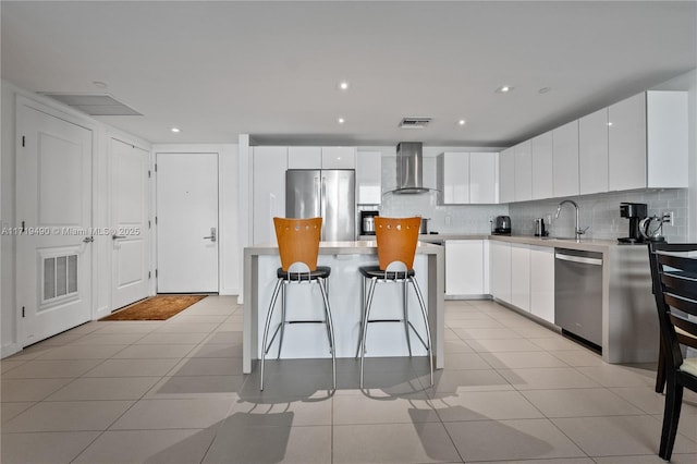 kitchen with wall chimney exhaust hood, stainless steel appliances, light tile patterned floors, white cabinets, and a center island