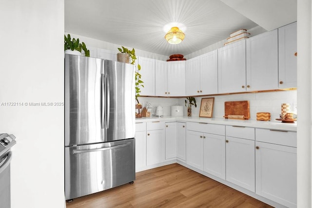 kitchen with light wood-type flooring, white cabinetry, stainless steel refrigerator, and tasteful backsplash