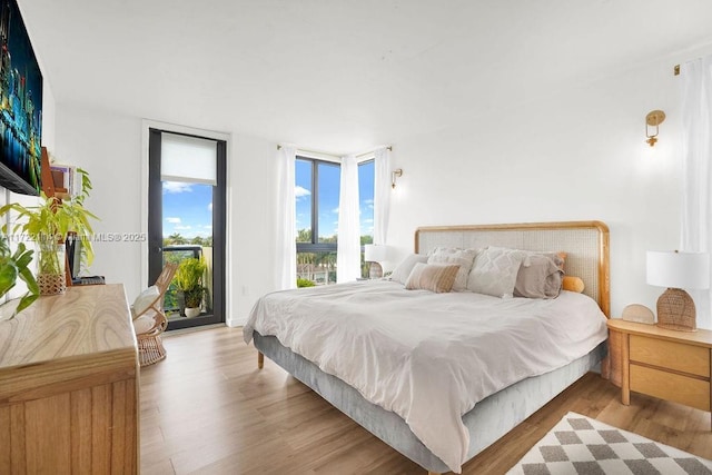 bedroom featuring light wood-type flooring, access to outside, and floor to ceiling windows