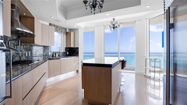 kitchen featuring stainless steel gas stovetop, a center island, an inviting chandelier, a water view, and wall chimney exhaust hood