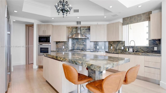 kitchen featuring wall oven, a tray ceiling, dark stone countertops, a kitchen island, and a breakfast bar area