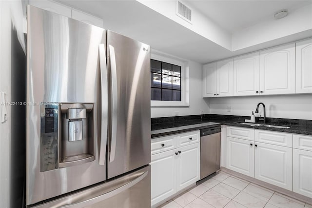 kitchen featuring stainless steel appliances, dark stone countertops, white cabinetry, and sink