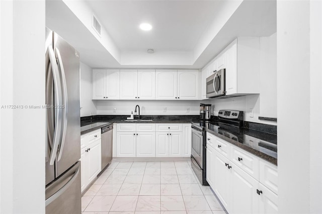 kitchen with sink, a tray ceiling, stainless steel appliances, white cabinets, and dark stone counters