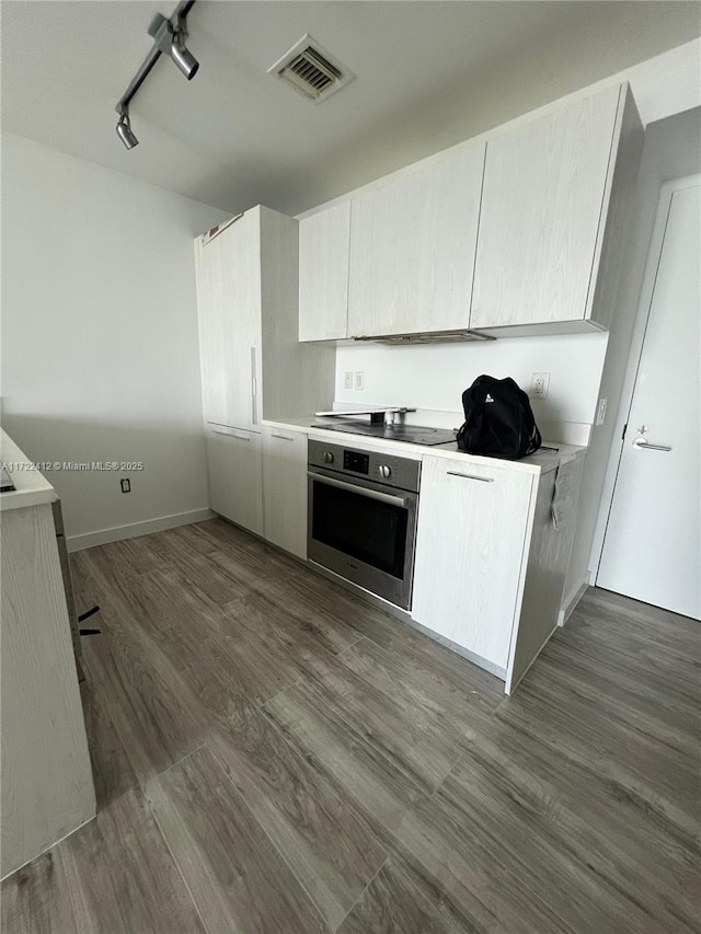 kitchen with cooktop, oven, dark wood-type flooring, and track lighting