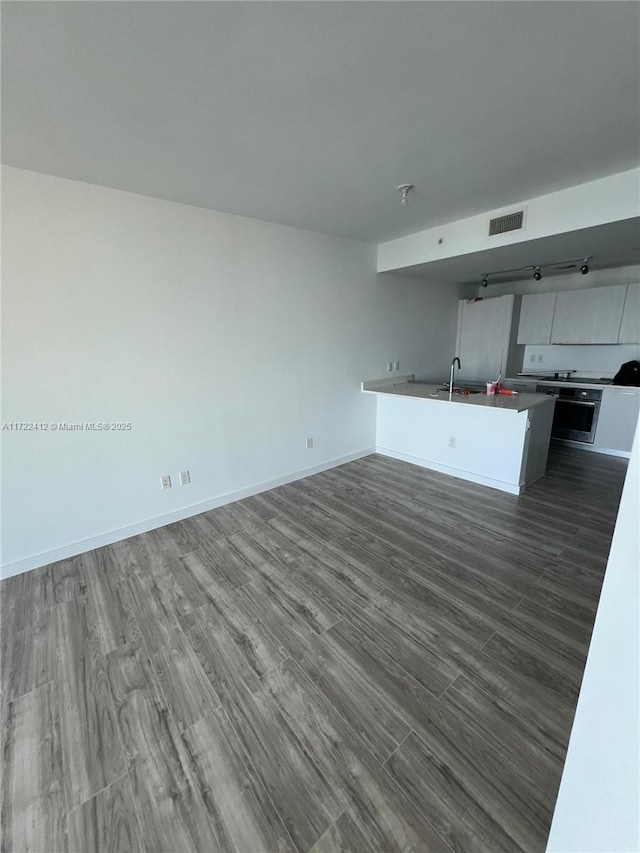 kitchen with kitchen peninsula, sink, stainless steel oven, and dark hardwood / wood-style floors