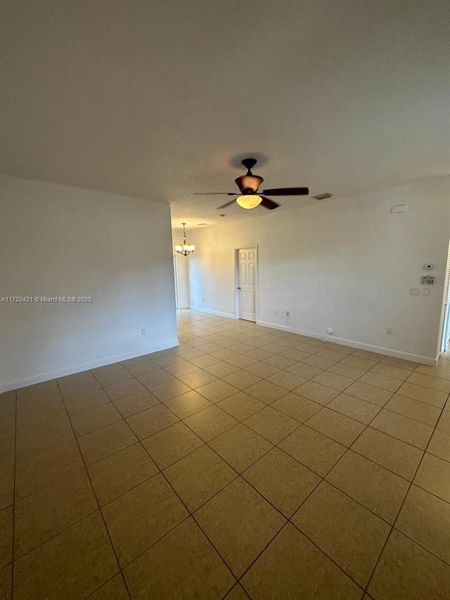 tiled empty room with ceiling fan with notable chandelier