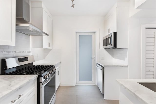 kitchen featuring light stone countertops, white cabinetry, stainless steel appliances, and wall chimney range hood