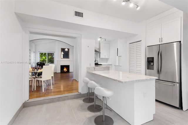 kitchen with a breakfast bar, kitchen peninsula, stainless steel fridge with ice dispenser, light stone counters, and white cabinetry