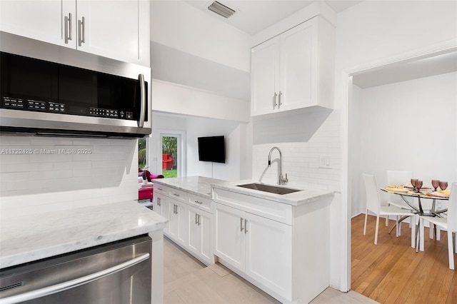 kitchen featuring light stone countertops, appliances with stainless steel finishes, tasteful backsplash, sink, and white cabinets