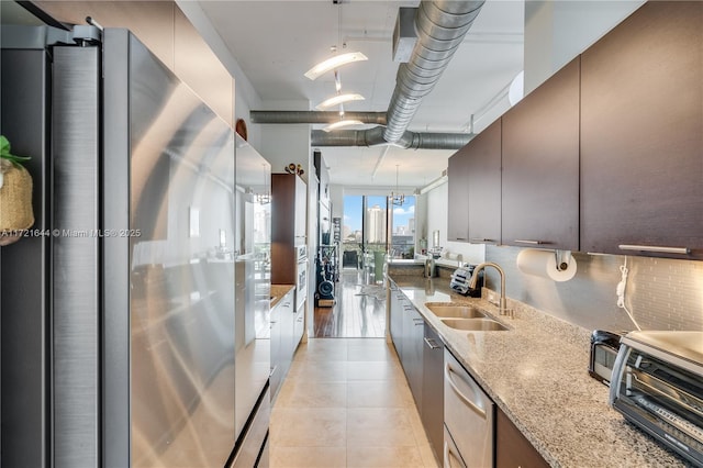 kitchen with pendant lighting, appliances with stainless steel finishes, sink, light stone counters, and light tile patterned floors