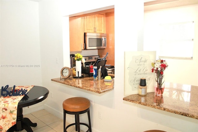 kitchen with light brown cabinetry, light stone counters, a breakfast bar, and light tile patterned floors