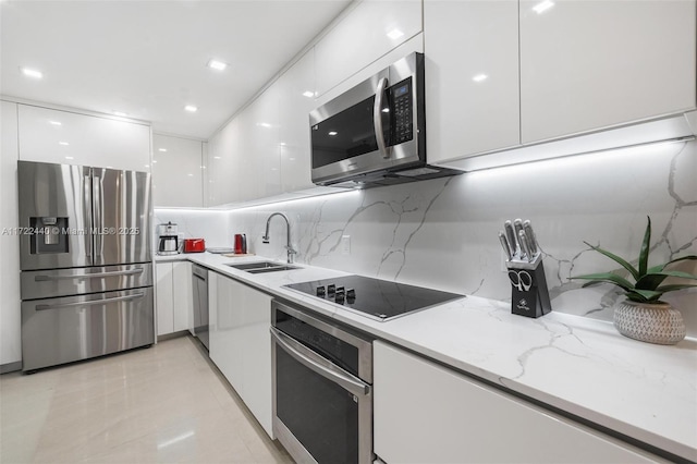 kitchen with light stone countertops, appliances with stainless steel finishes, tasteful backsplash, sink, and white cabinetry