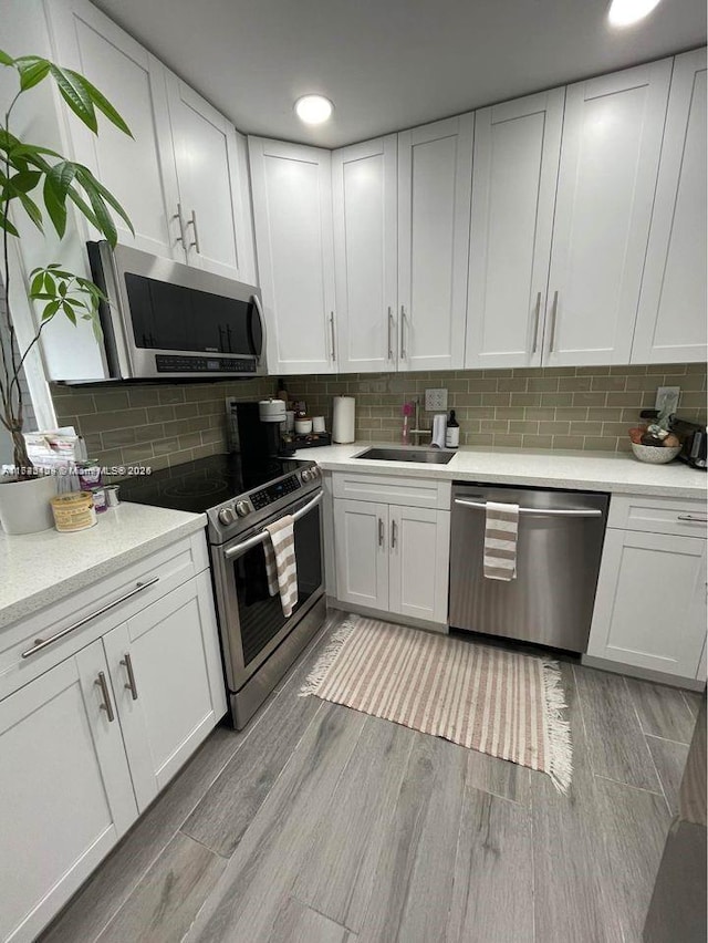 kitchen featuring backsplash, stainless steel appliances, sink, light hardwood / wood-style flooring, and white cabinets