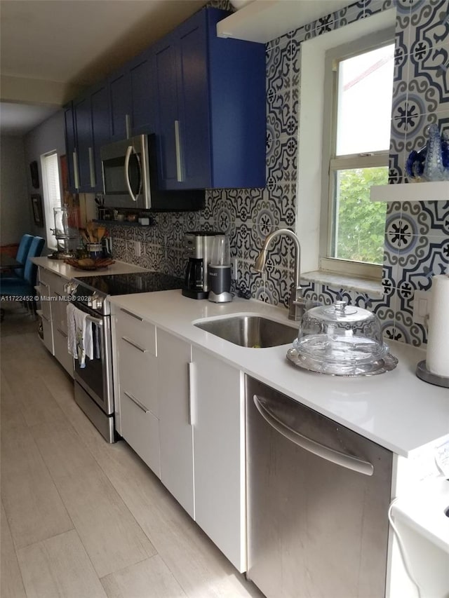 kitchen with backsplash, white cabinets, sink, blue cabinetry, and stainless steel appliances