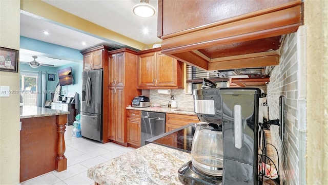 kitchen featuring ceiling fan, stainless steel appliances, light stone counters, decorative backsplash, and light tile patterned flooring