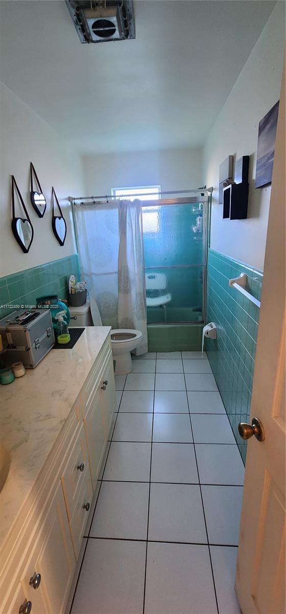 full bathroom featuring tile patterned floors, shower / bath combination, toilet, vanity, and tile walls