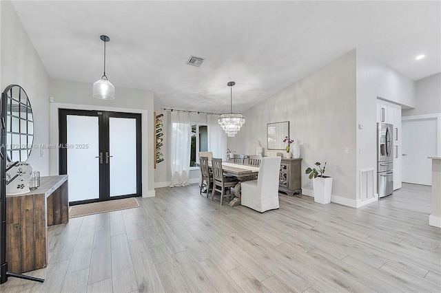 dining area with french doors, a chandelier, and light wood-type flooring