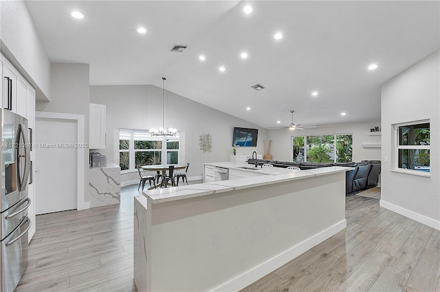 kitchen featuring light stone countertops, stainless steel appliances, pendant lighting, vaulted ceiling, and ceiling fan with notable chandelier