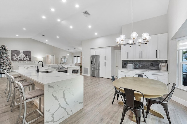 kitchen with light stone countertops, white cabinetry, sink, stainless steel appliances, and decorative light fixtures