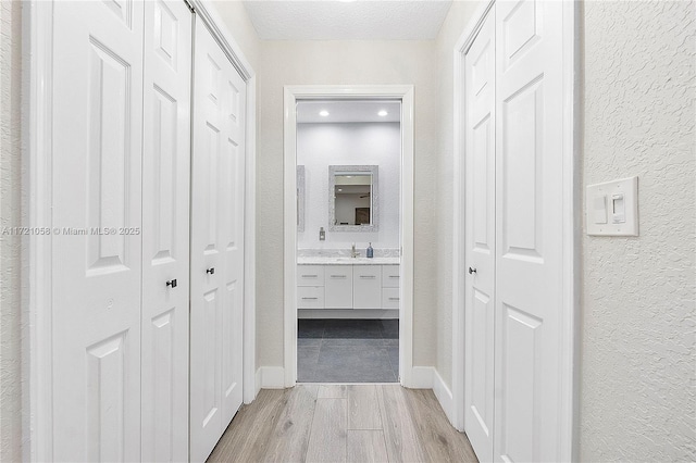 corridor with sink, a textured ceiling, and light wood-type flooring