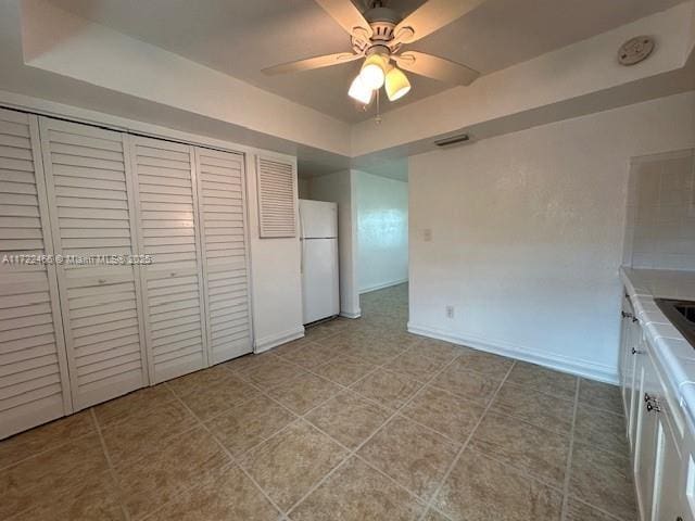 unfurnished bedroom with white refrigerator, a closet, ceiling fan, and a tray ceiling