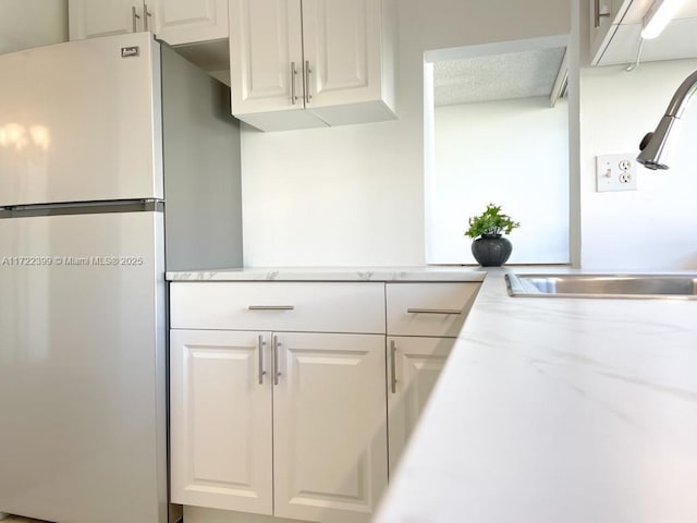 kitchen featuring white cabinets, stainless steel refrigerator, and sink